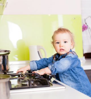 Cute boy playing with the gas stove by himself. Small boy left alone in the kitchen, playing with the gas stove. Baby boy standing near the stove looking into the camera